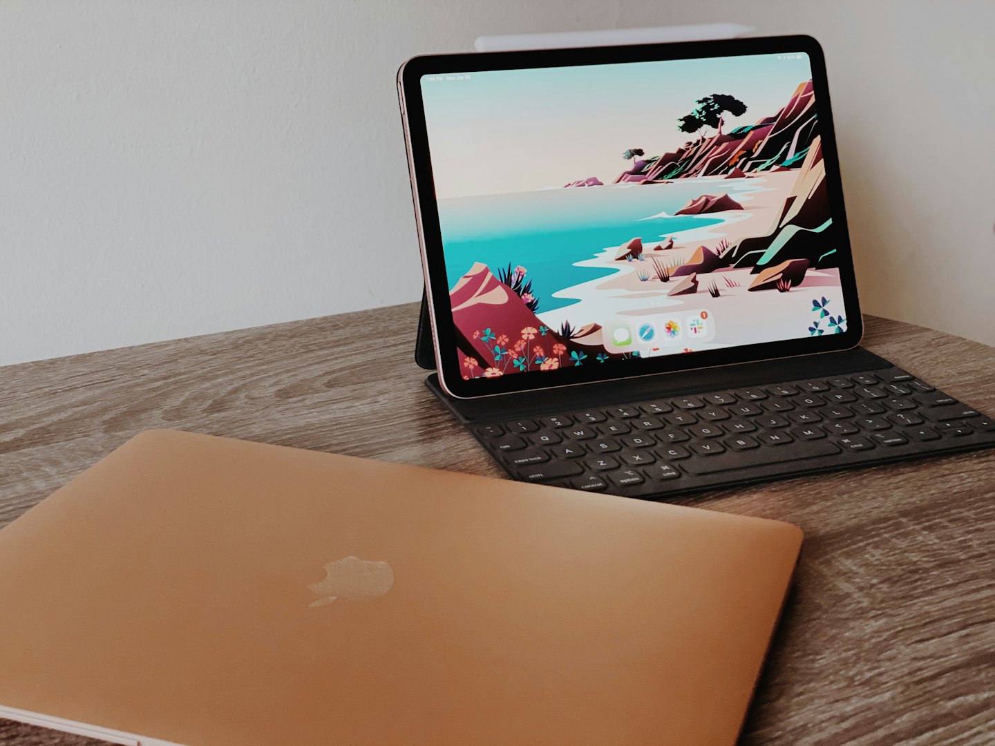 Laptop and tablet on a wooden desk with white wall.