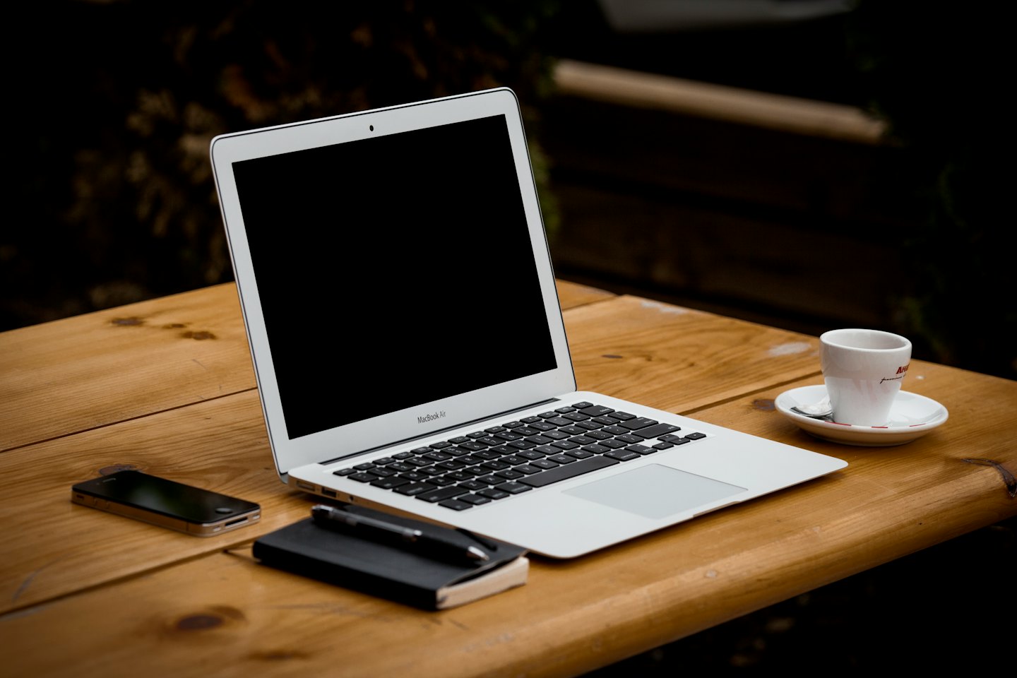 Open laptop with smartphone and notebook on wooden table.